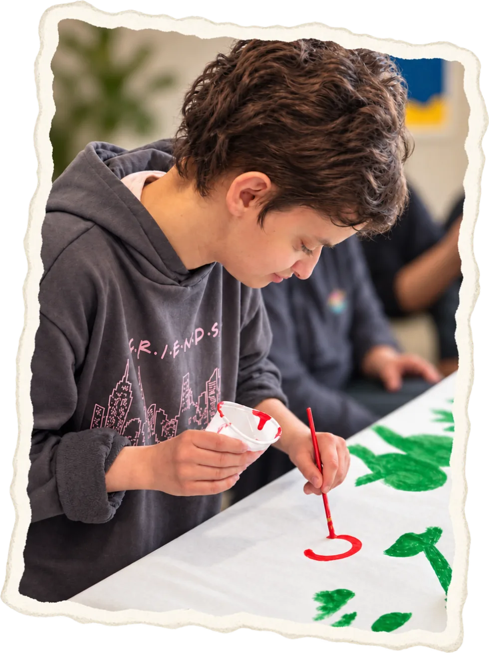 A young person in a grey hoodie painting onto a long paper banner
