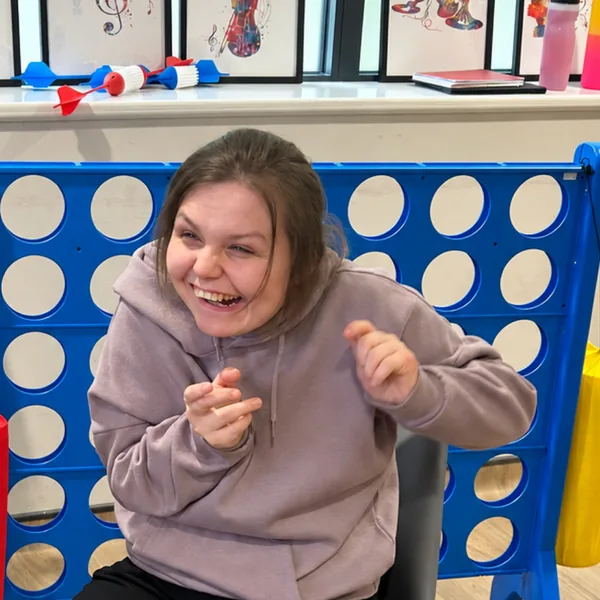 A young woman laughing in the activities room, in front of a giant Connect 4 game