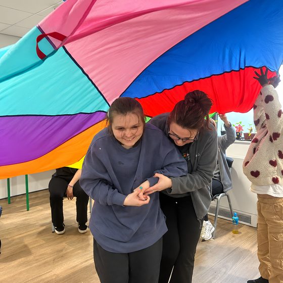 Members and staff playing with a colourful parachute game in the activities room.