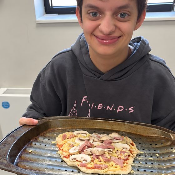 A member smiling while holding a tray with their home-made pizza.