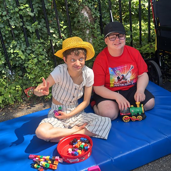 Two young people playing with toys on a mat outdoors in the sunshine.